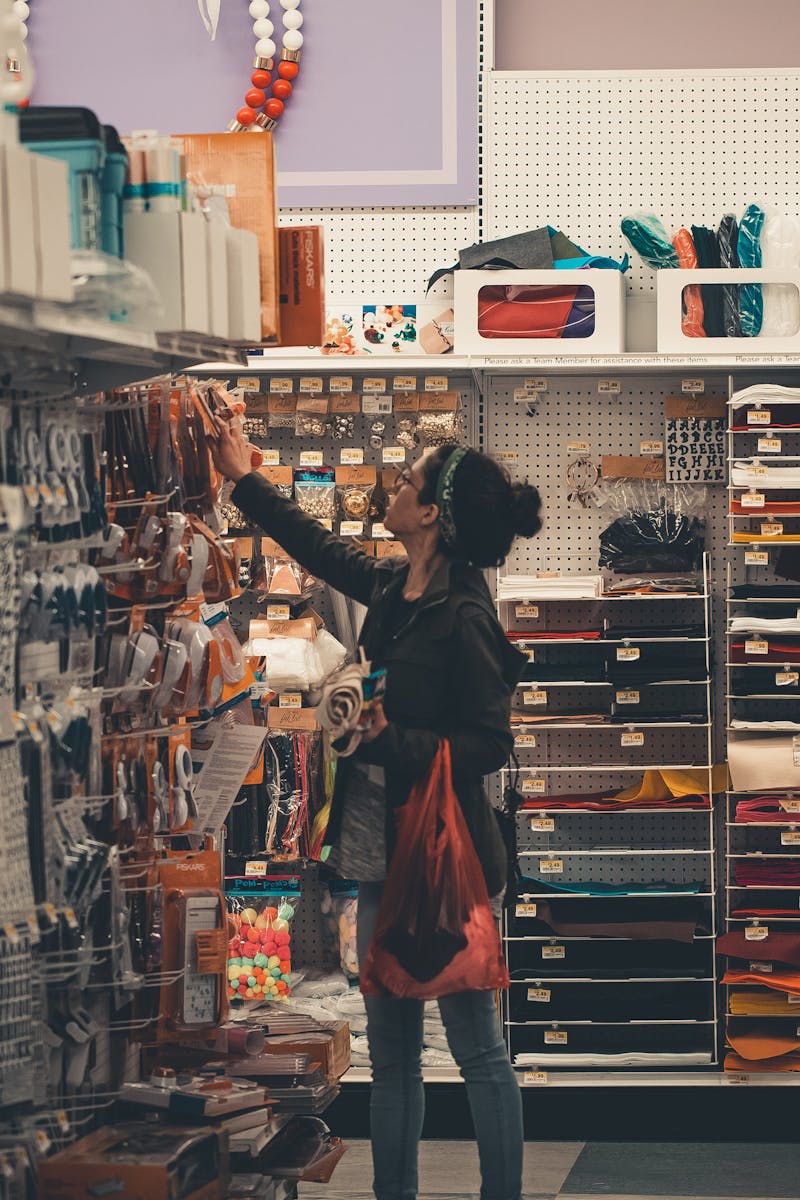 Woman reaching for items in a busy craft store aisle, exploring various art supplies.