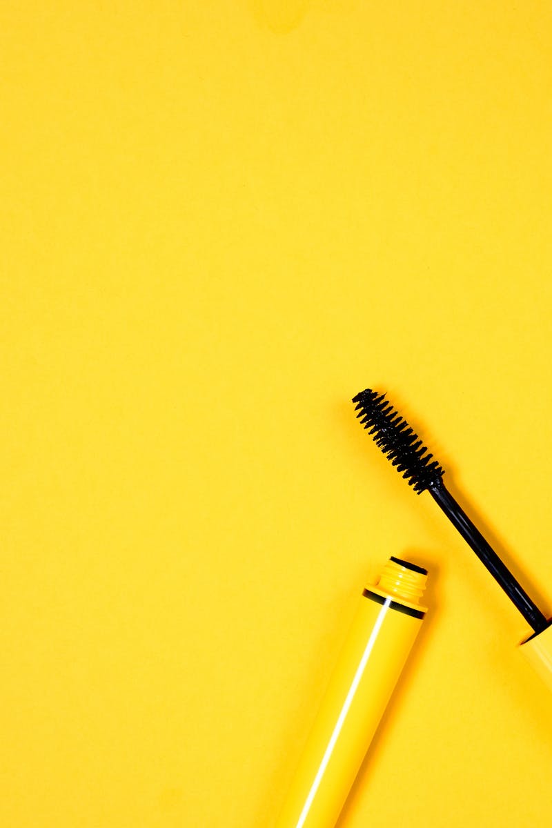 Open mascara with brush on vibrant yellow background, perfect for beauty and cosmetic themes.